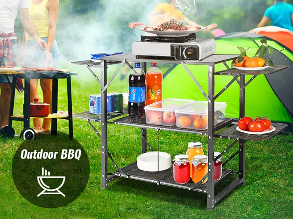 Mesa de cocina para acampar VEVOR con barbacoa, comida, bebidas y una carpa verde al fondo.