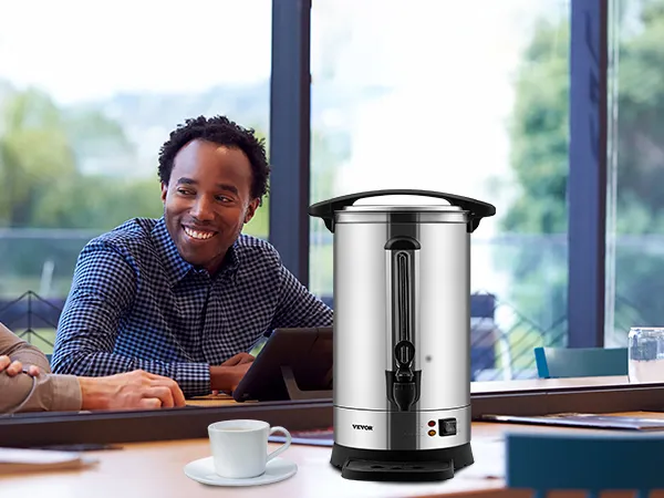 Cafetera VEVOR sobre una mesa de reuniones con gente, una taza de café y granos de café derramados cerca.