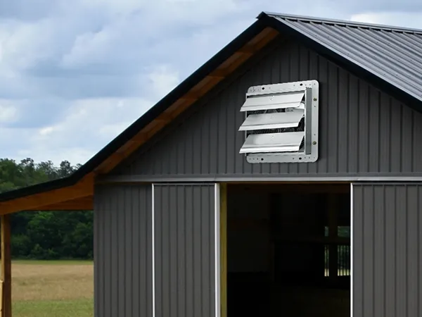 gray barn with VEVOR shutter exhaust fan installed, set against a backdrop of trees and a cloudy sky.