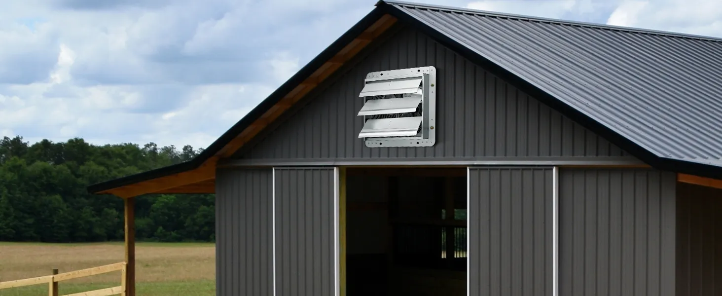 gray barn with VEVOR shutter exhaust fan installed, set against a backdrop of trees and a cloudy sky.