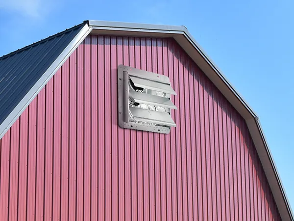 red barn with VEVOR shutter exhaust fan installed on upper wall under clear blue sky.