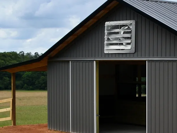 VEVOR shutter exhaust fan installed on a gray barn with a metal roof under cloudy sky.