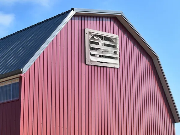 red barn with a VEVOR shutter exhaust fan on the side under a clear blue sky.