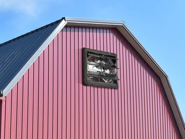 Exterior de granero con un extractor de aire con persiana VEVOR montado en una pared de metal rojo contra un cielo azul.
