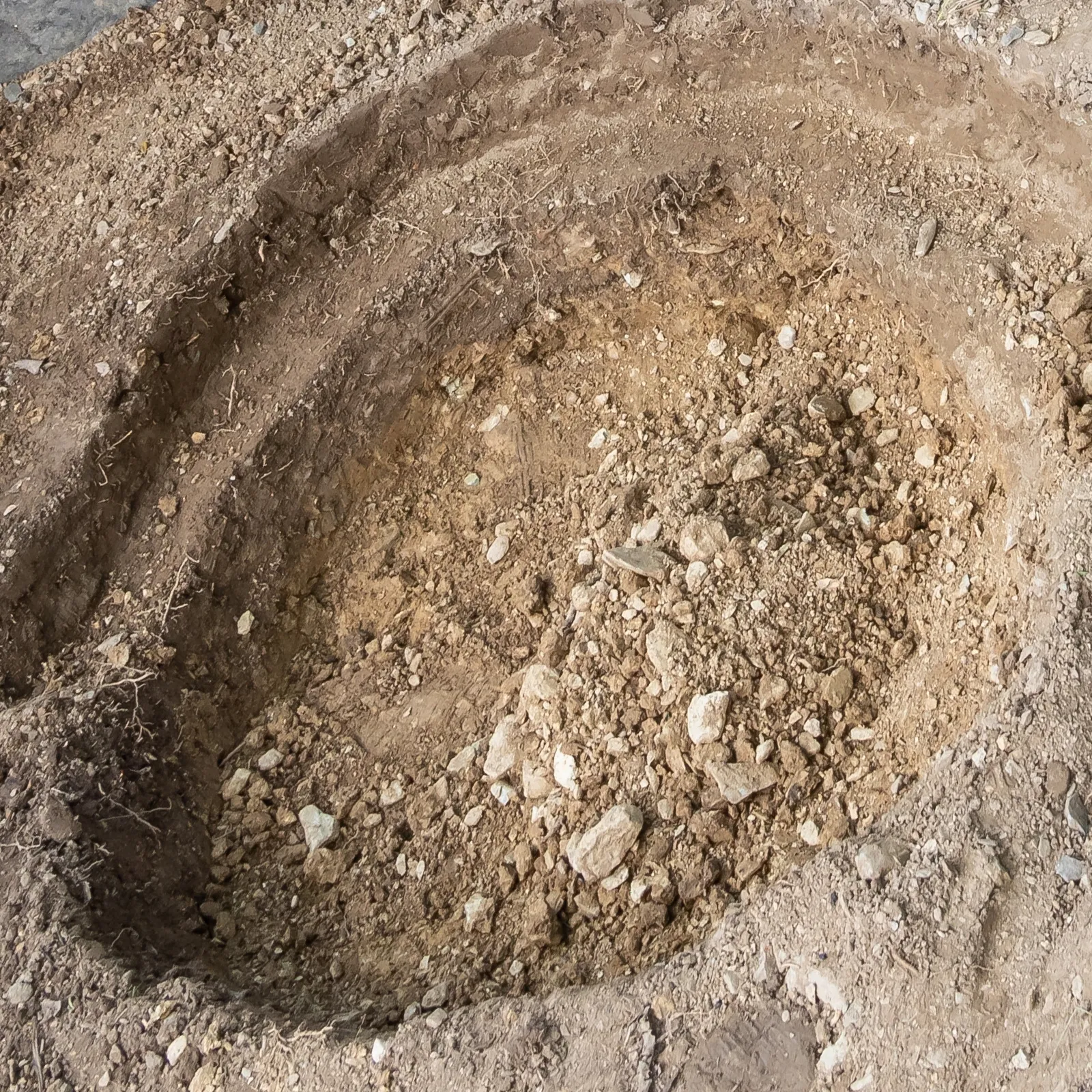 ground excavation site prepared for VEVOR pond liner installation, showing layers of soil and rocks.