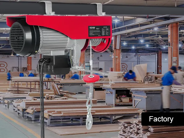 Polipasto eléctrico VEVOR en entorno de fábrica con materiales de madera y trabajadores al fondo.