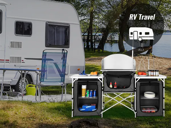 VEVOR camping kitchen table setup by an rv with chairs near a lake, surrounded by trees.