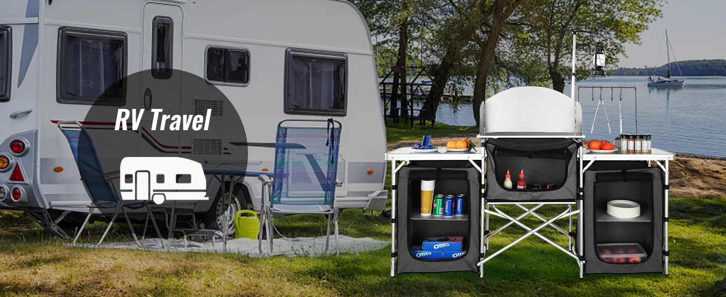 VEVOR camping kitchen table setup by an rv with chairs near a lake, surrounded by trees.