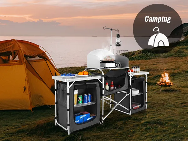 VEVOR camping kitchen table set up near a tent by the sea with supplies and food for outdoor cooking.