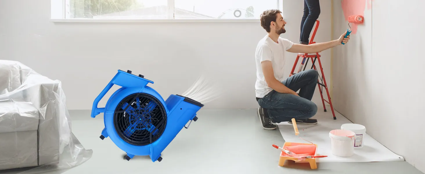 Soplador de piso VEVOR en uso durante la pintura de la pared, sofá cubierto, suministros de pintura en el piso.