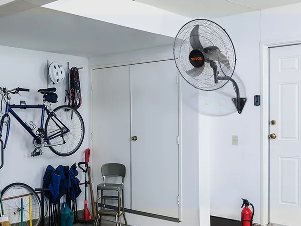 garage with VEVOR wall mount fan, bicycles, a metal chair, and storage units against a white wall.