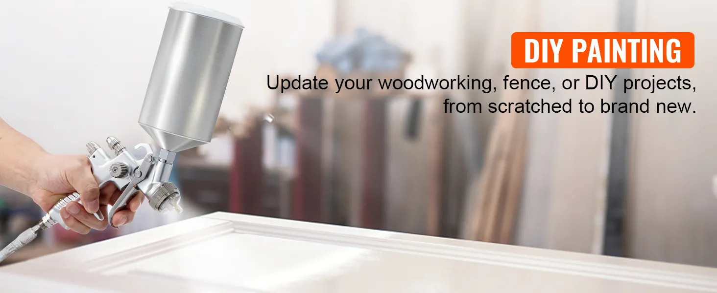 mano sosteniendo una pistola rociadora de pintura para automóviles VEVOR, pintando una superficie blanca con texto de pintura de bricolaje en el fondo.