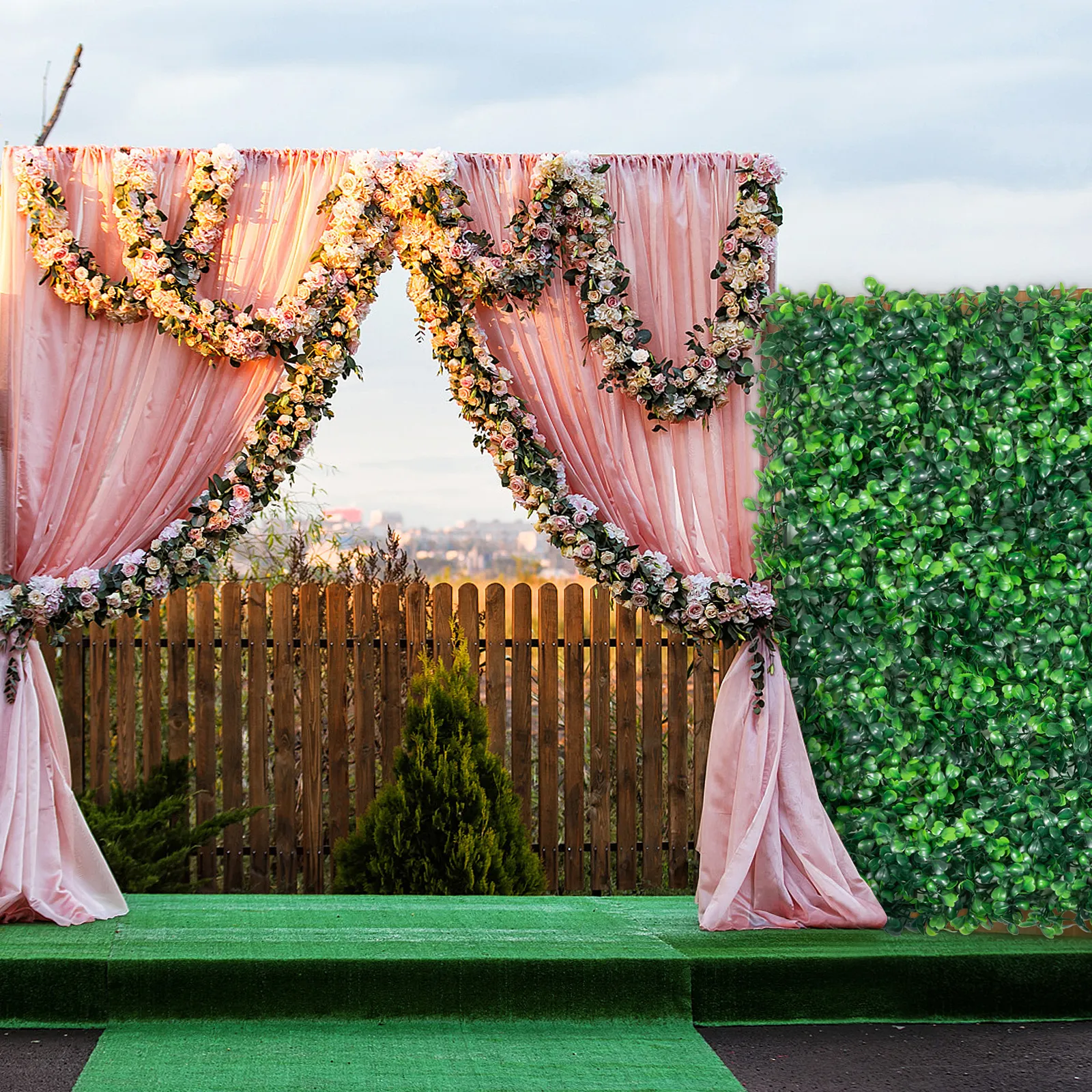 pastel pink floral arch with drapery, wooden fence, and VEVOR artificial boxwood panel.