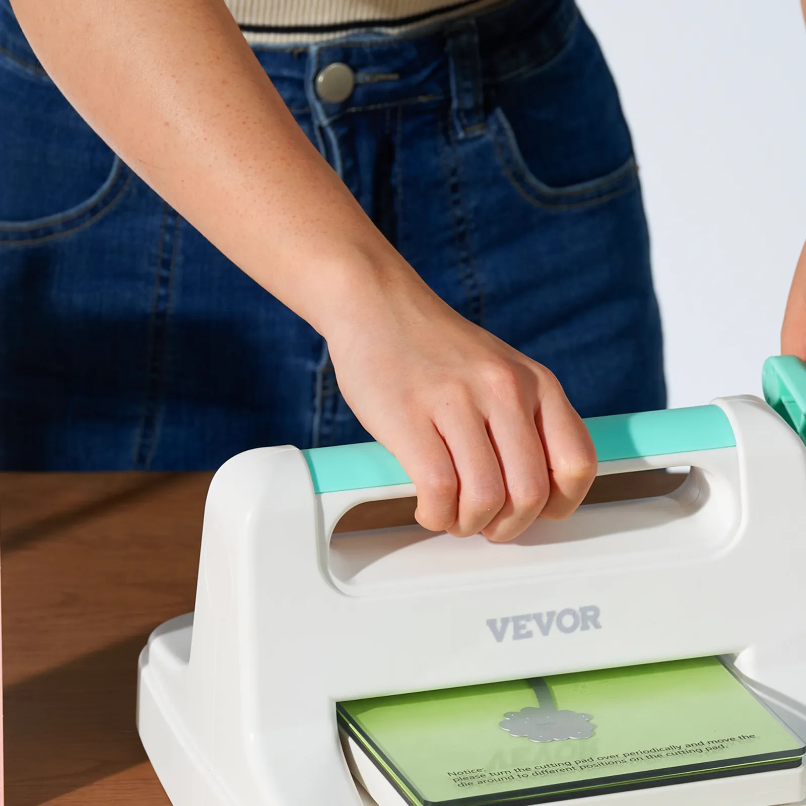 person using VEVOR die cutting machine with blue handle and green cutting mat. denim jeans background.