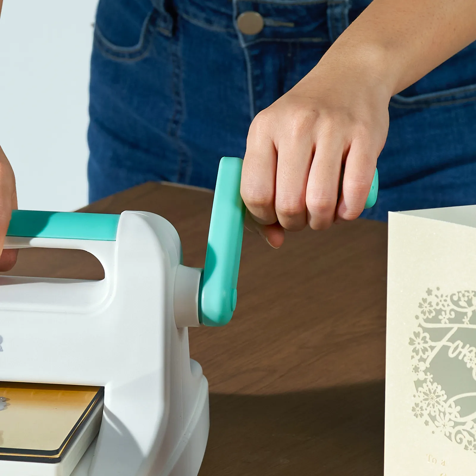 hand operating VEVOR die cutting machine next to a decorated card on a wooden table.