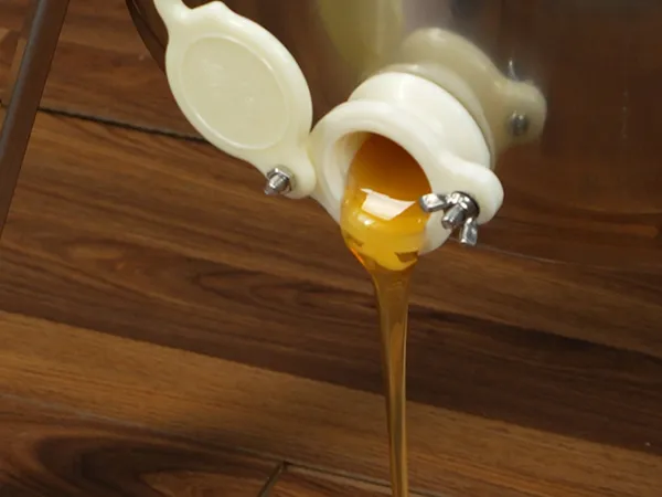 honey flowing from a stainless steel VEVOR honey extractor onto a wooden surface.
