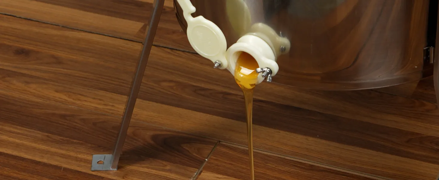 honey flowing from a stainless steel VEVOR honey extractor onto a wooden surface.