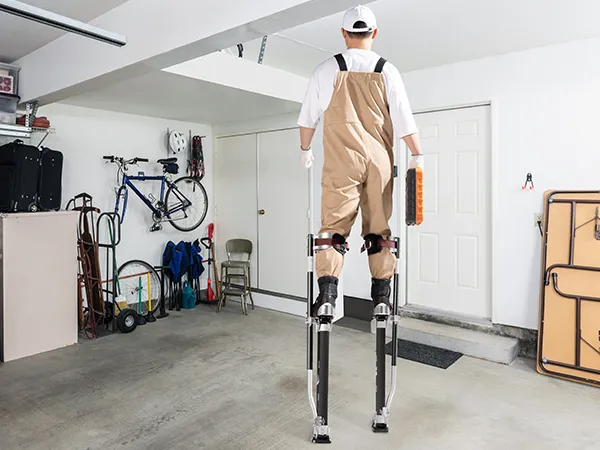 worker on VEVOR drywall stilts painting walls in garage and installing ceiling in under-construction room.
