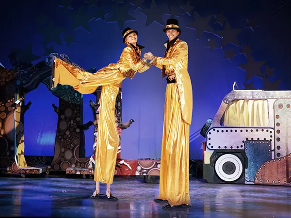 performers in gold costumes on stilts in front of a colorful stage set, wearing VEVOR drywall stilts.