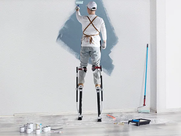 painter using VEVOR drywall stilts to paint a wall, surrounded by painting tools and supplies.