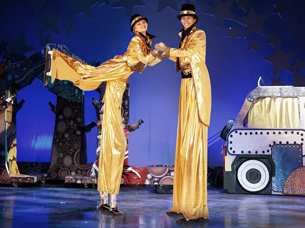 performers in golden outfits on VEVOR drywall stilts, dancing on a colorful stage set with starry backdrop.