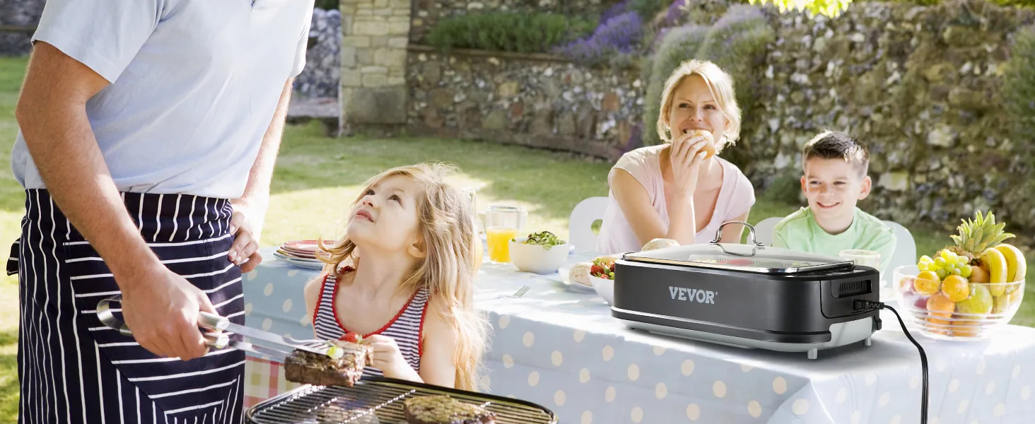 Familia disfrutando de una barbacoa al aire libre con una parrilla interior sin humo VEVOR sobre una mesa, con un frutero colorido cerca.