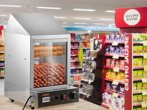 Vaporera para hot dogs VEVOR en un mostrador en el pasillo bien iluminado de una tienda de comestibles con bocadillos en el fondo.