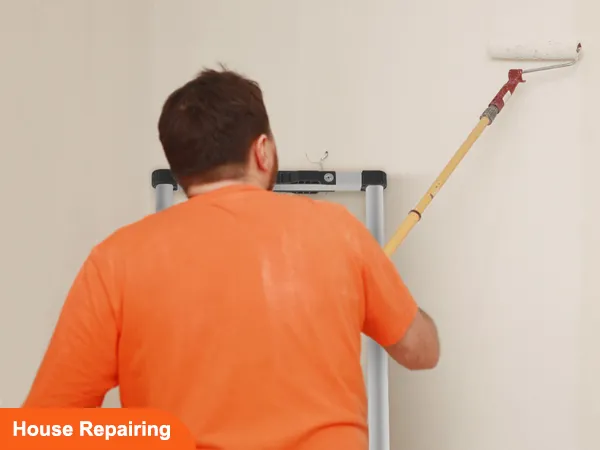Mann benutzt Farbrolle an Wand, steht auf VEVOR-Teleskopleiter, Hausreparatur im Gange.