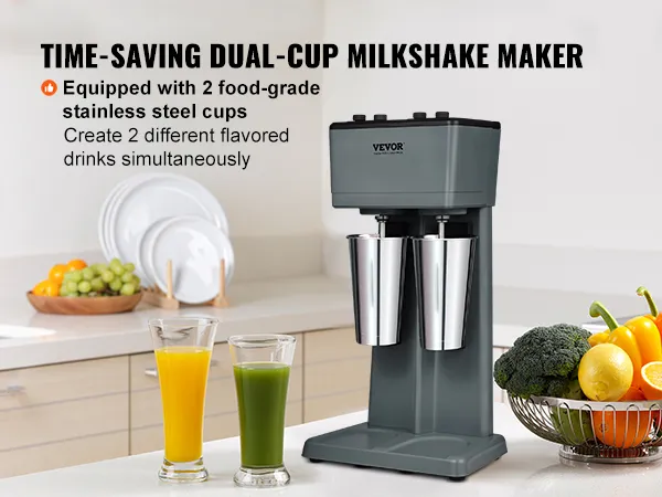 Máquina para hacer batidos VEVOR en una cocina moderna con dos tazas de acero inoxidable y verduras frescas cerca.