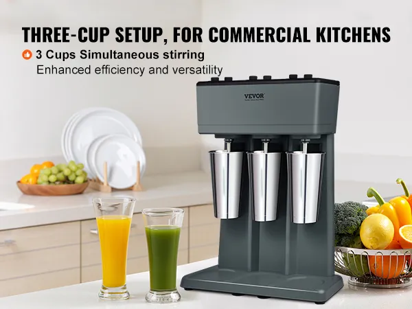 Máquina para hacer batidos VEVOR en una cocina con tres tazas de acero inoxidable y verduras frescas en la encimera.