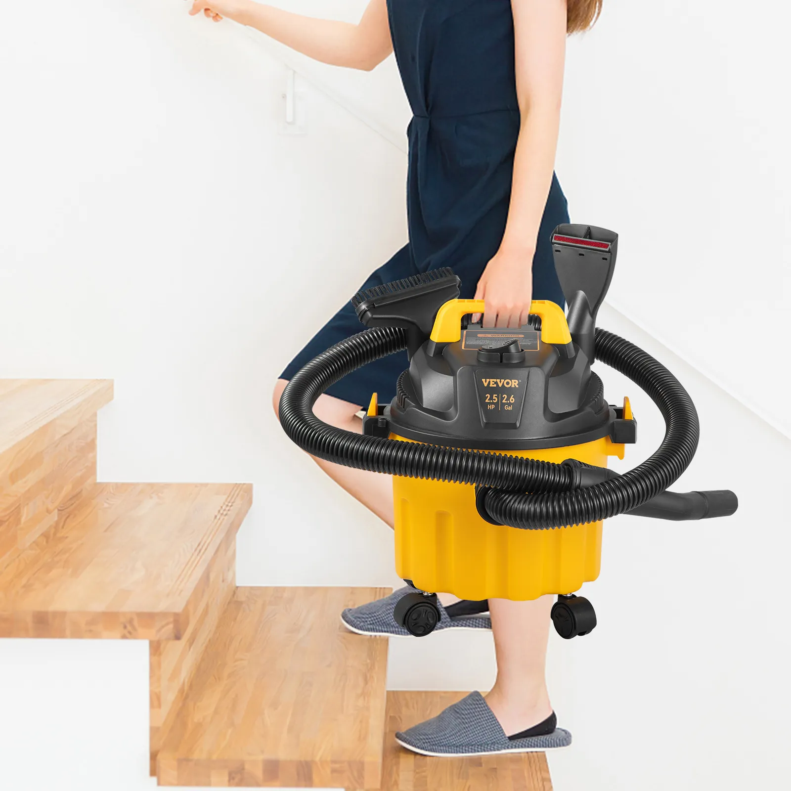 person carrying VEVOR wet dry vac up wooden stairs in a bright, minimalist indoor setting.