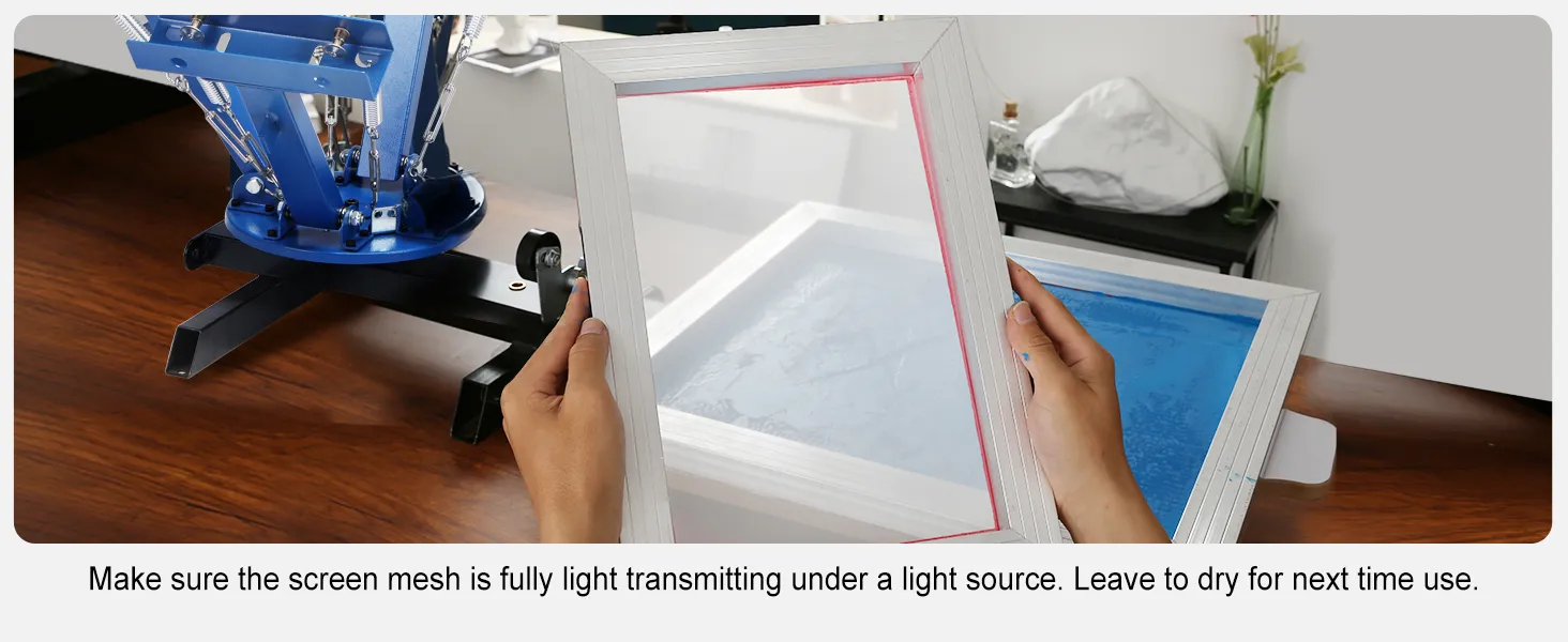 hands holding a white frame, VEVOR screen printing kit on a wooden table with a blue machine in background.