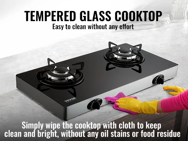 Cocina a gas VEVOR con vidrio templado, limpiada por una persona con sudadera rosa y guantes amarillos.
