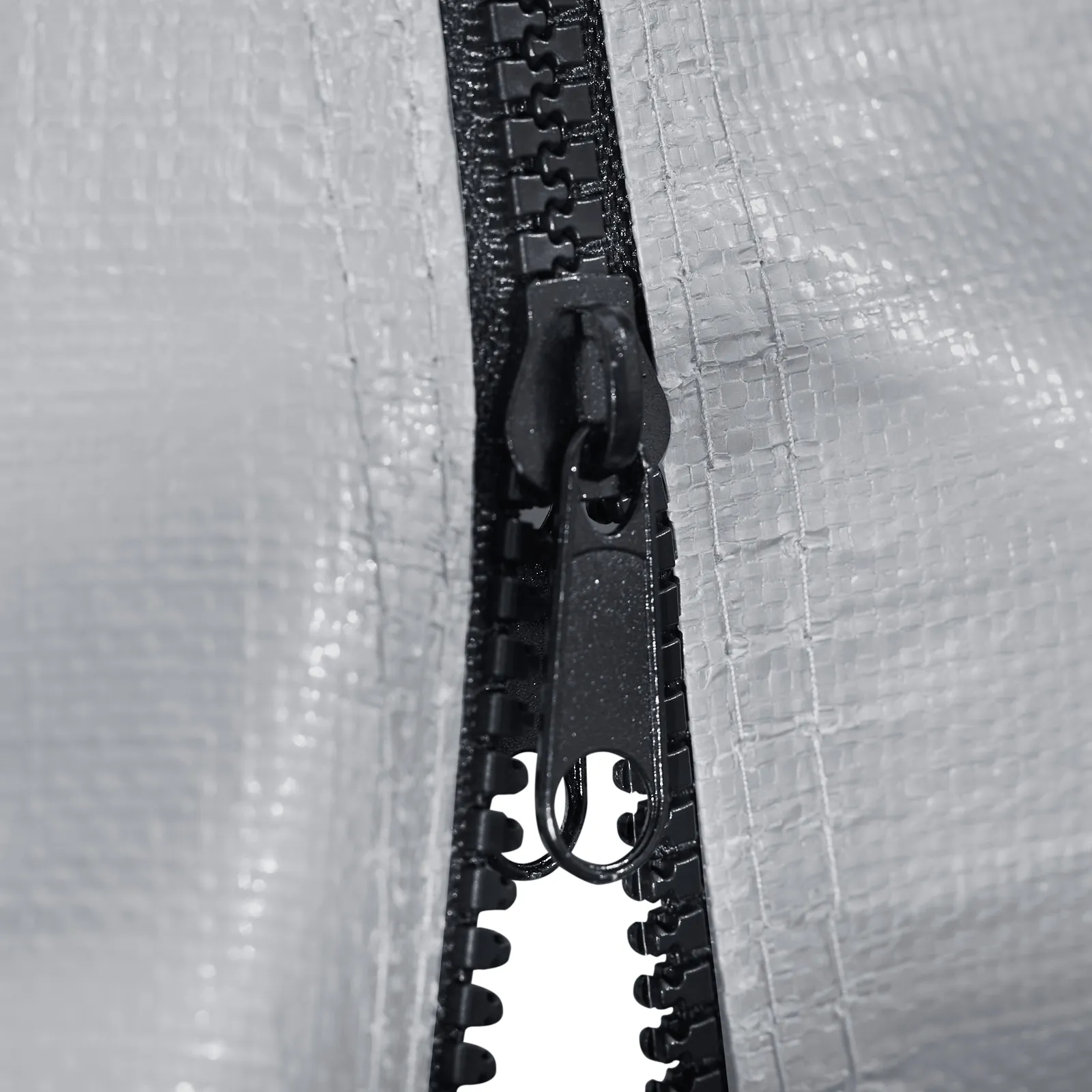 Primer plano de una cremallera gris en un cobertizo portátil VEVOR con un fondo de tela texturizada.