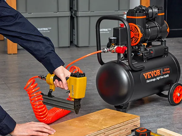 Persona que utiliza una pistola de clavos conectada a un compresor de aire ultra silencioso VEVOR con una manguera naranja enrollada.