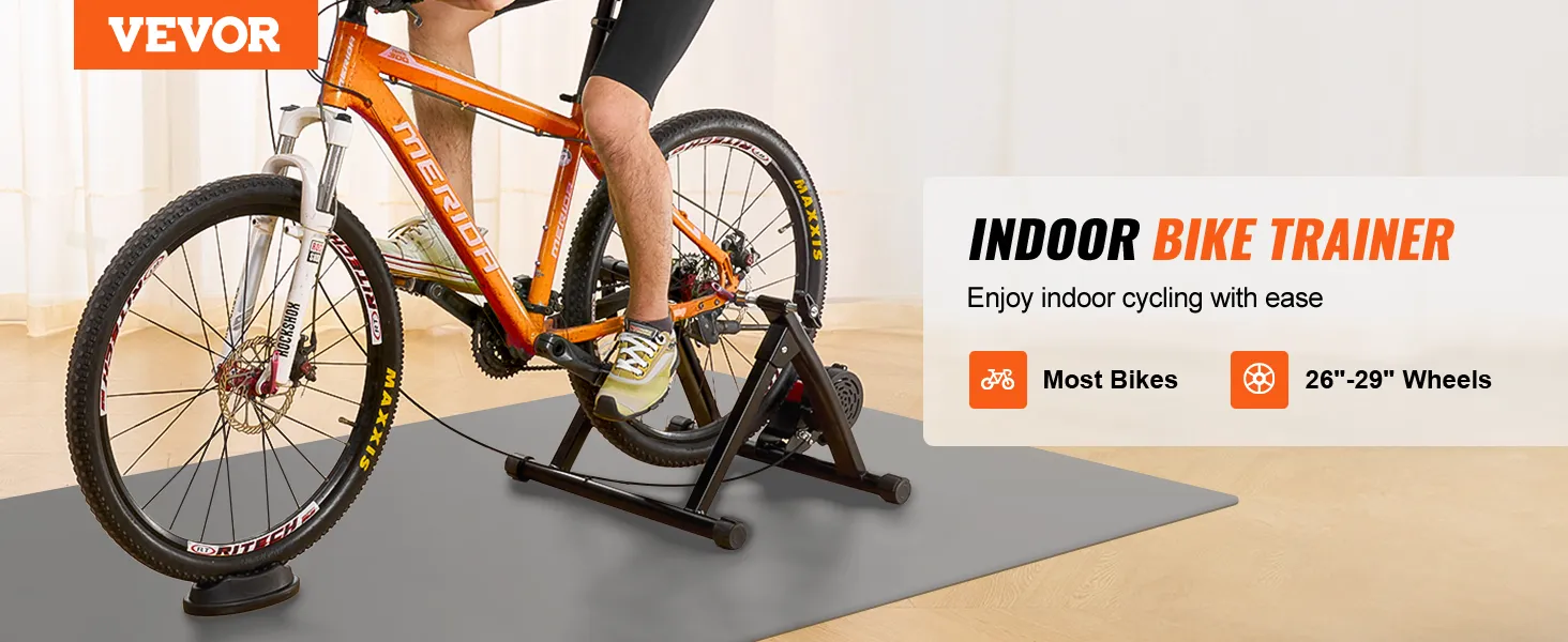 cyclist using the VEVOR bike trainer stand for indoor biking with an orange bike on a hardwood floor.