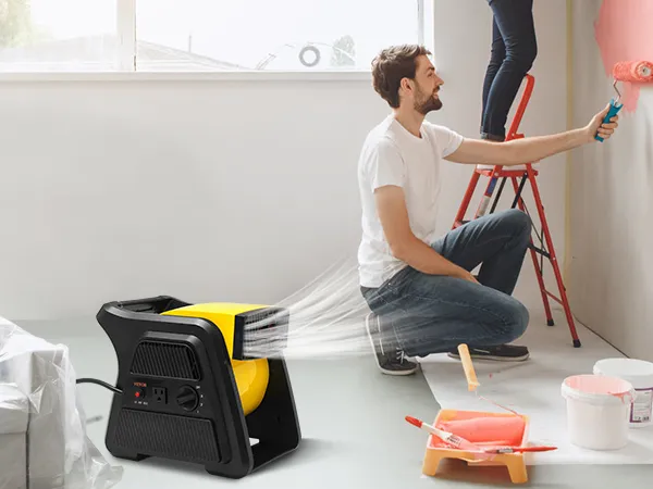 Escena de renovación del hogar con ventilador multiuso VEVOR, hombre pintando una pared, mujer en una escalera y muebles cubiertos.