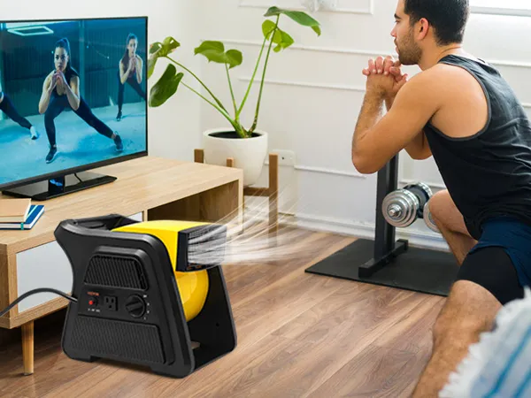Hombre haciendo ejercicio en casa con un ventilador multiusos VEVOR que proporciona ventilación y un televisor que muestra un video de ejercicios.