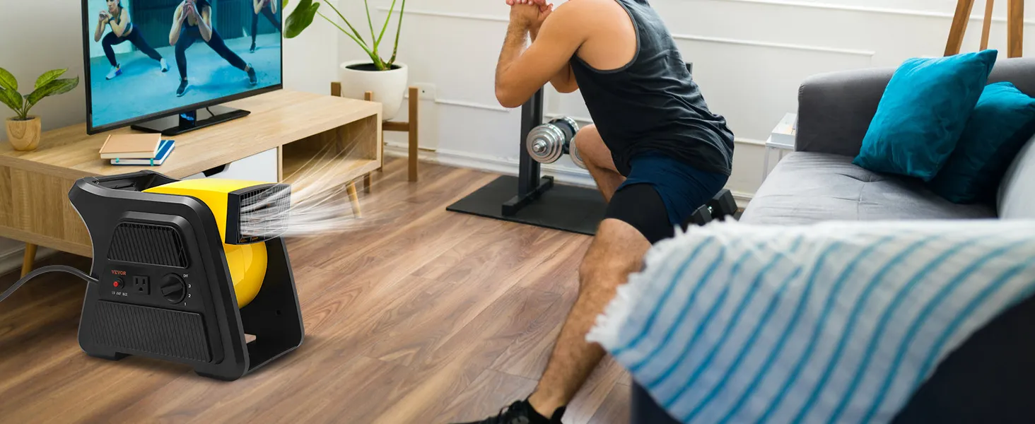 Hombre haciendo ejercicio en casa con un ventilador multiusos VEVOR que proporciona ventilación y un televisor que muestra un video de ejercicios.