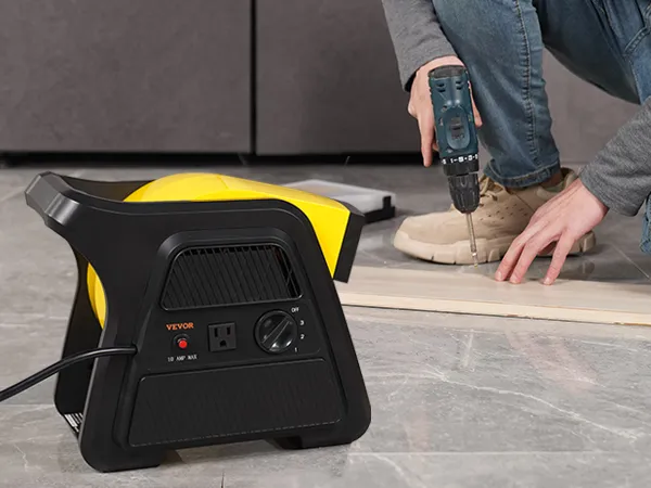 Trabajador que utiliza un taladro junto a un ventilador utilitario VEVOR colocado sobre un suelo de baldosas grises.