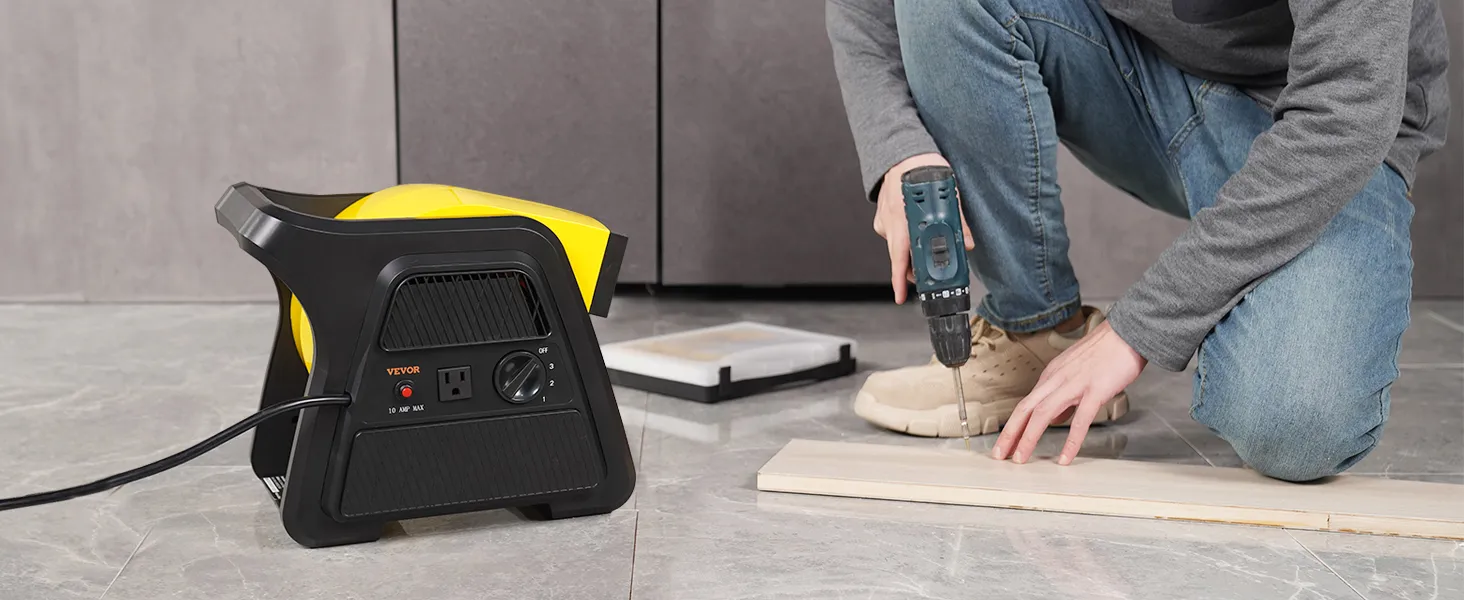 Trabajador que utiliza un taladro junto a un ventilador utilitario VEVOR colocado sobre un suelo de baldosas grises.
