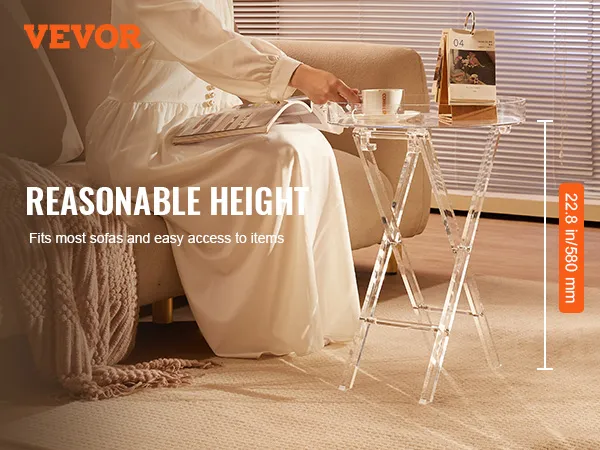 Klappbarer Tabletttisch aus Acryl von VEVOR neben einem Sofa. Eine Frau in einem weißen Kleid zeigt ihn lässig.