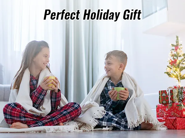 Niños con pijamas a cuadros disfrutan de bebidas cerca de un árbol de Navidad con regalos etiquetados como "regalo navideño perfecto".